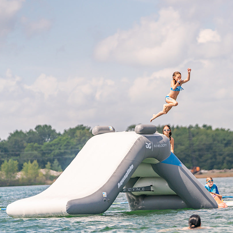 Child leaping off Velocity Slide 6.0 into lake as people watch on a sunny day.