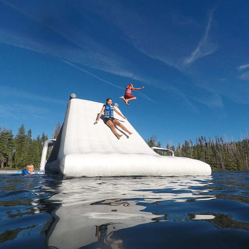 People enjoy the Velocity Slide 10.0 on a lake under a clear blue sky.