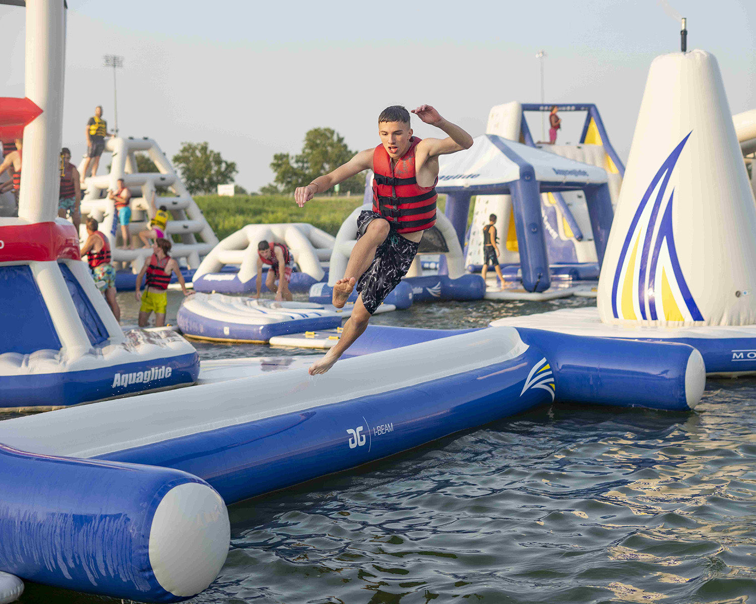 Person jumping on an inflatable water obstacle course, wearing a red life vest.