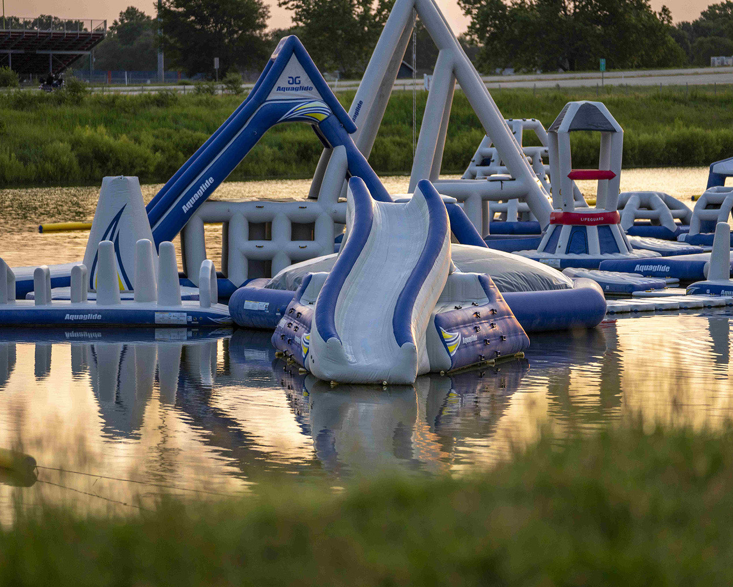 Inflatable water park on a calm lake with slides and climbing structures.