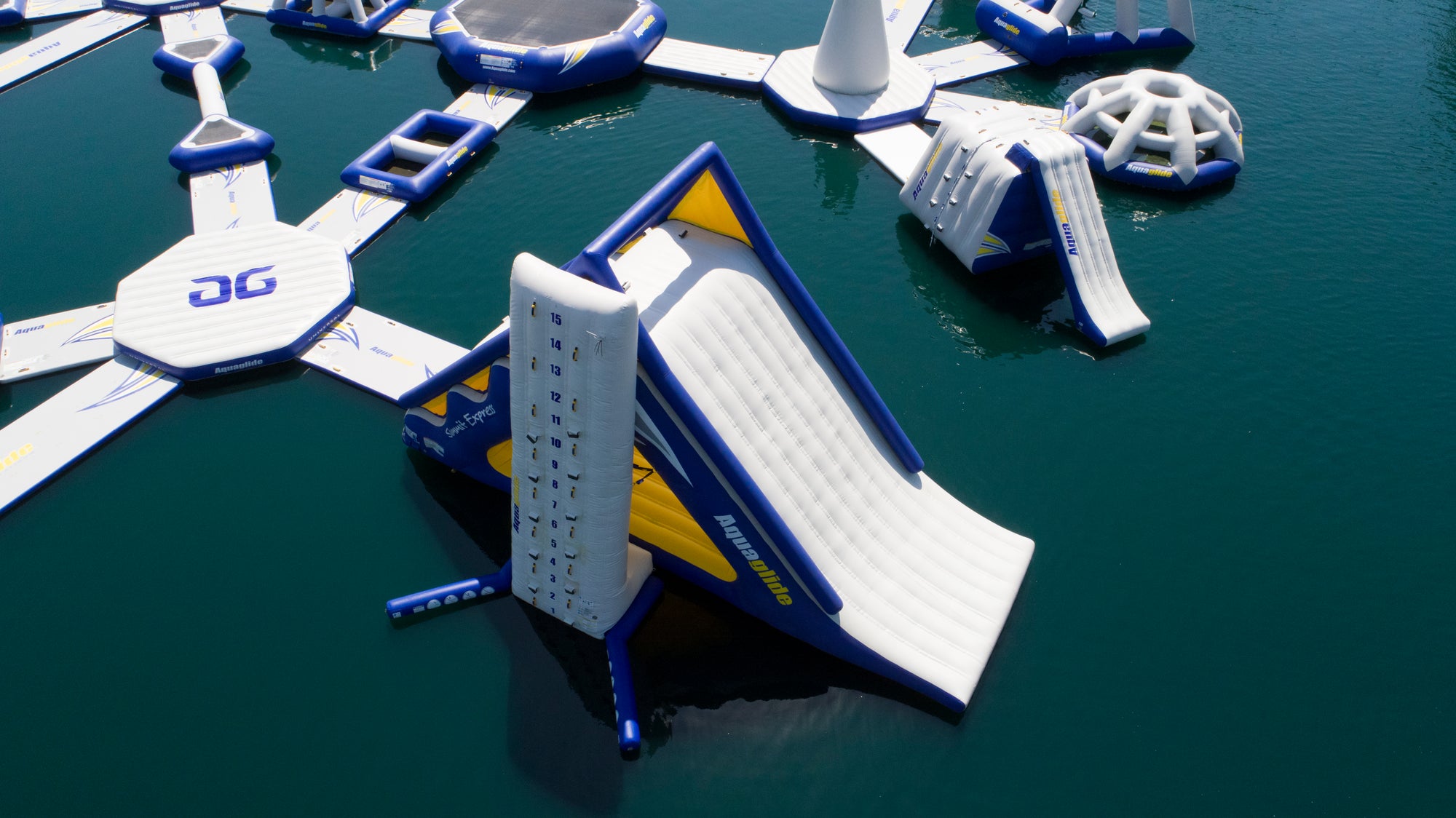 Floating inflatable water park with slides and climbing features on a calm lake.