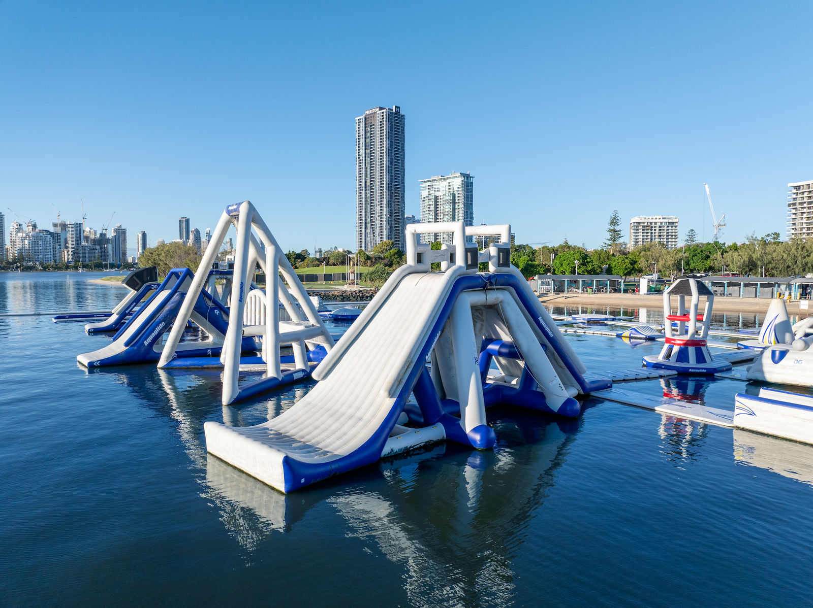 Aquaglide slides and towers floating near city buildings on a calm, sunny day.