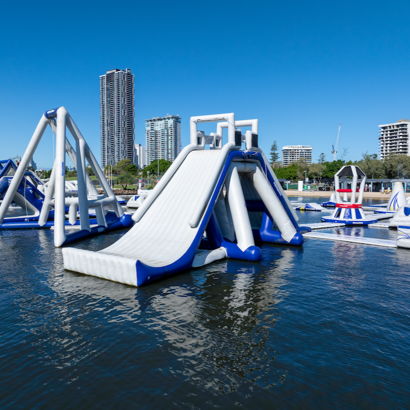 El Jefe inflatable slide with ladder and platform, floating on water in front of a city skyline.