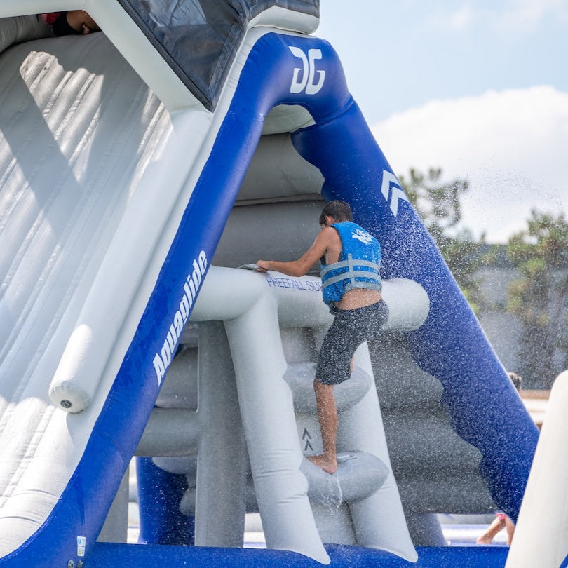 Swimmer climbing up the Supreme Freefall lakefront park wearing a blue life jacket.
