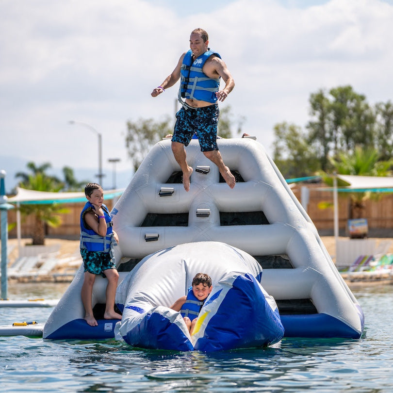 Dad wearing a blue life jacket jumping onto the Aquaglide Launch pad while his son waits to be launched into the lake while his other son looks on from the side.