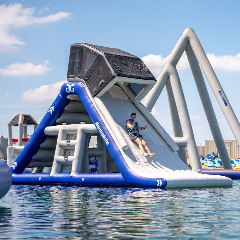 Side view of Aquaglide lakefront mini park with someone sliding down the slide into the lake, plugging is nose.