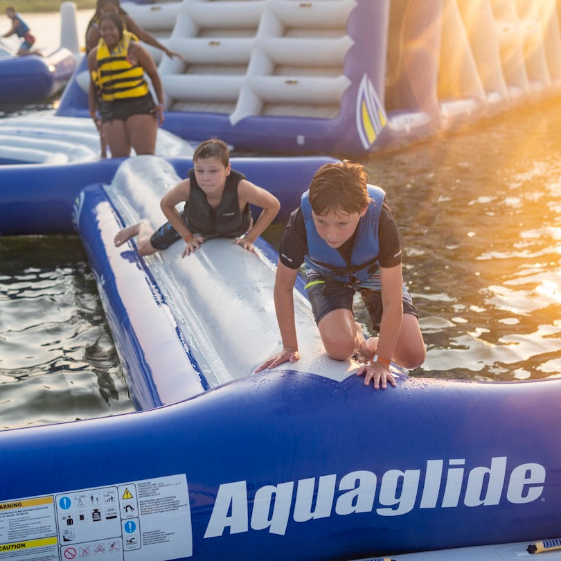 Two boys climb across the front of the Aquaglide I-Beam in the evening light.