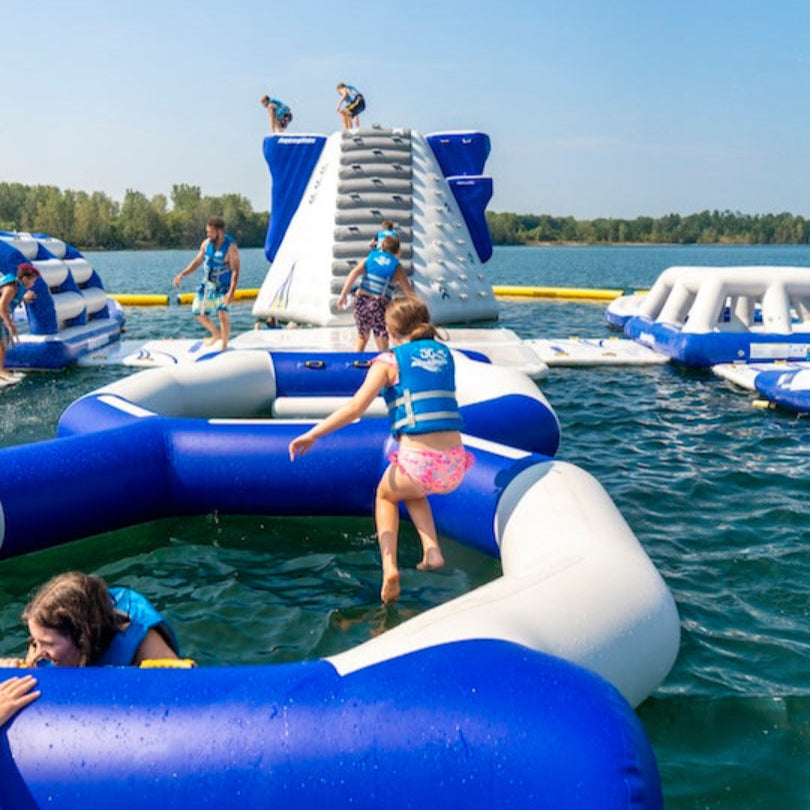 Children in life vests playing on Aquaglide Figure 8 inflatable over water.