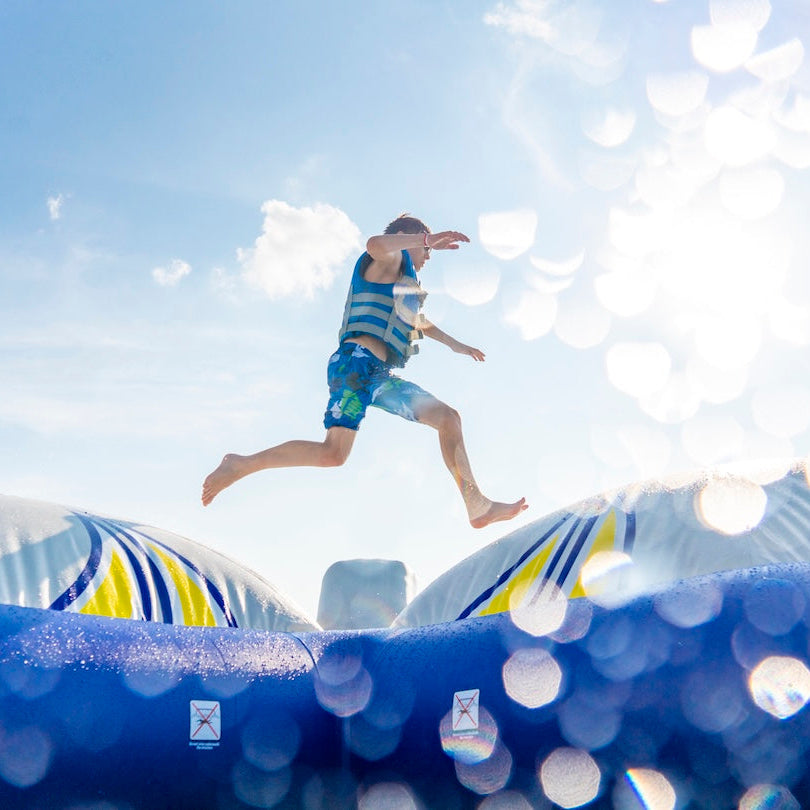 Boy mid-air between domes on the Double Icecap inflatable with sun flare in background.