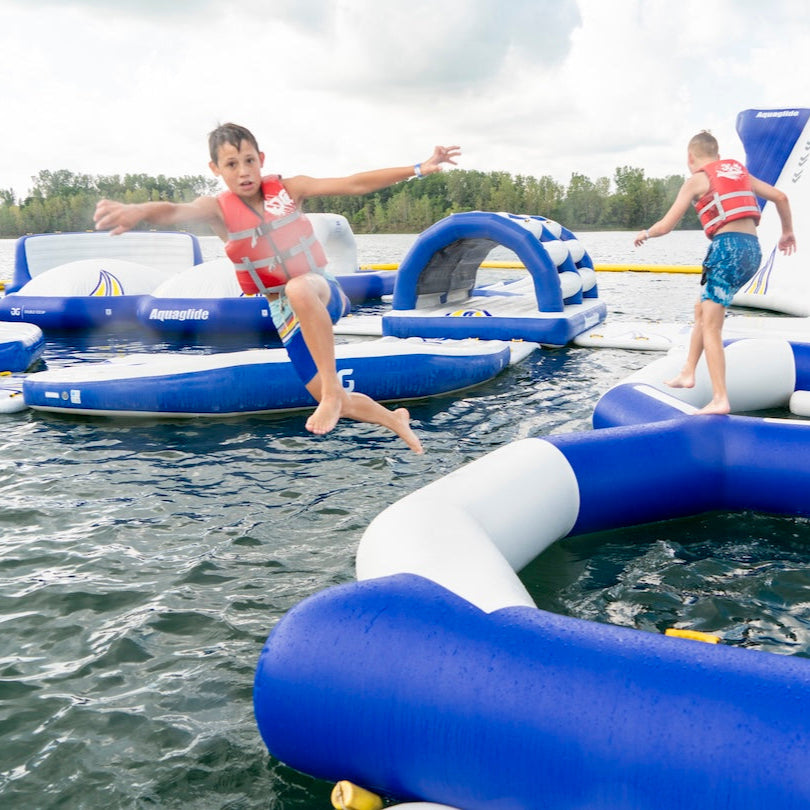 Boy mid-air jumping off Aquaglide Figure 8 with inflatables in background.