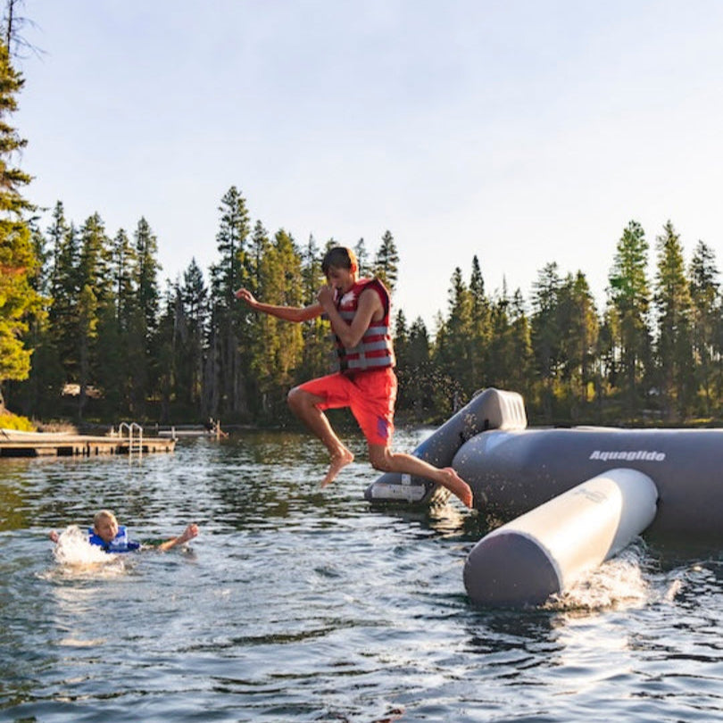 Young boy wearing red Aquaglide life jacket jumping off of the Recoil balance beam into the lake.