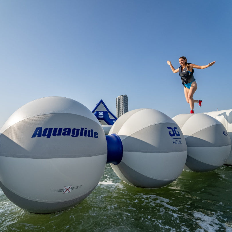 Person balancing on inflatable Helix obstacle over water on a sunny day.