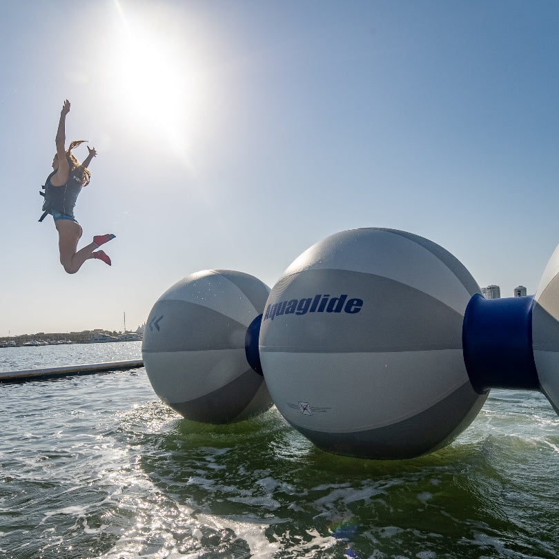 Person jumping off an inflatable Helix water obstacle into the water under bright sunlight.