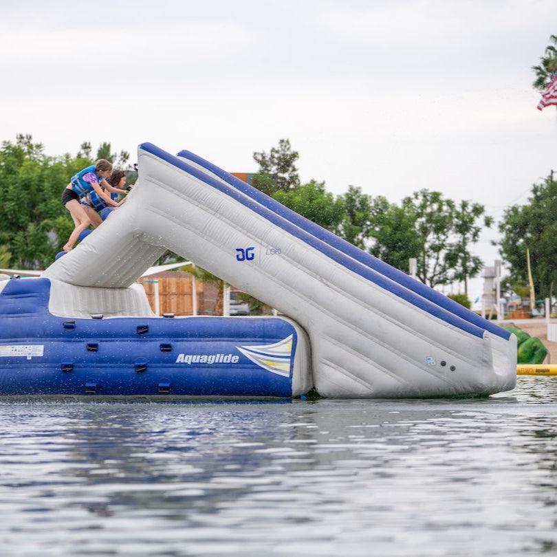 Kids in life vests climb the side of the Loki inflatable slide at a waterfront water park.