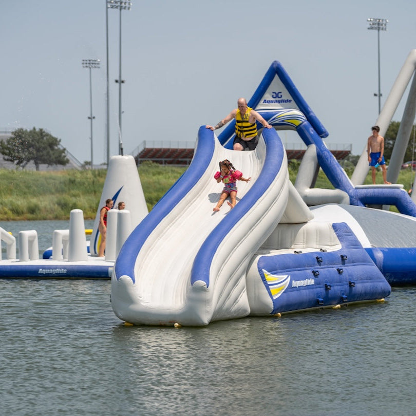Adult and child in vests go down the Loki inflatable slide with water features in the background.