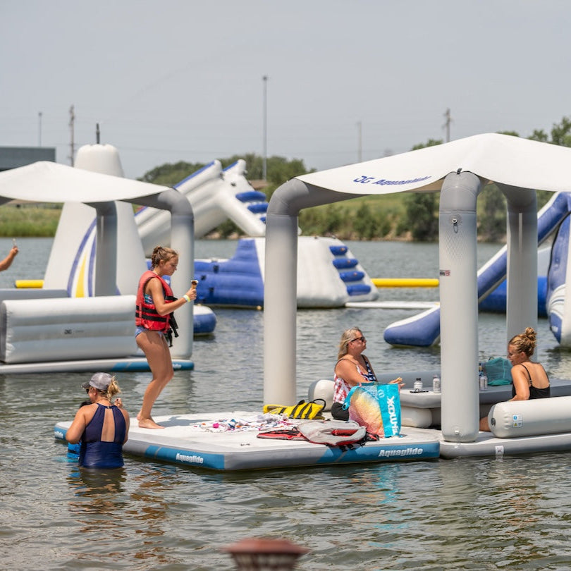 People enjoy a sunny day on the Solarium inflatable lounges on a lake.