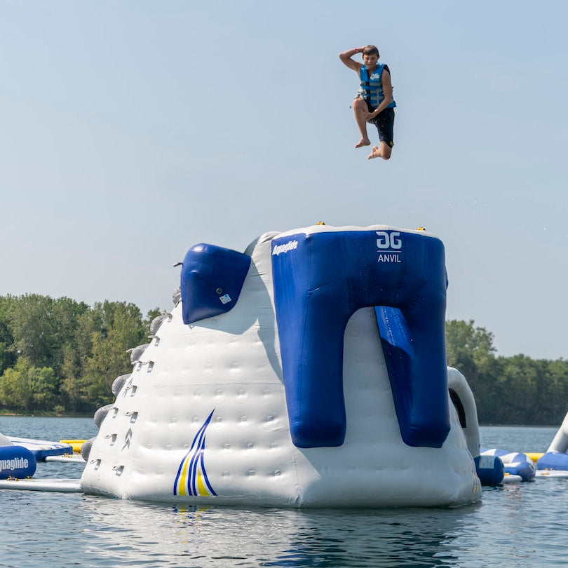 Child jumping off the Aquaglide Anvil inflatable jumping platform wearing a blue life jacket and striking a pose.