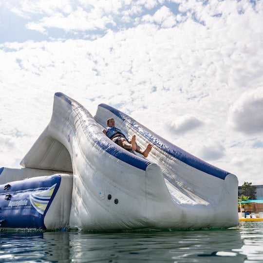 Man in a life vest slides down the Loki inflatable under a bright sky with scattered clouds.