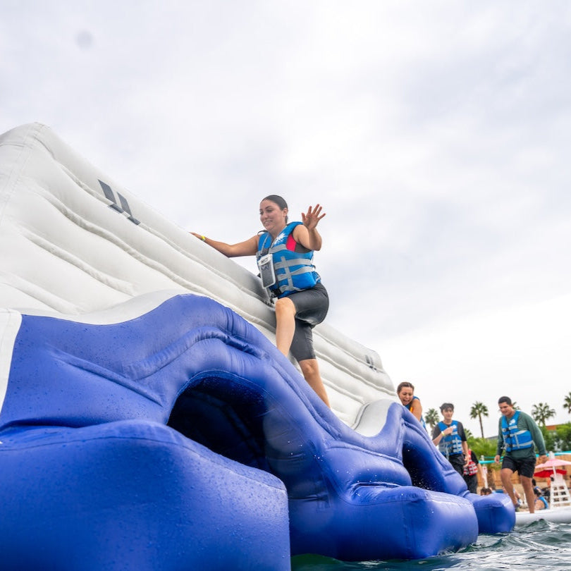 Woman in a life vest steps up the Arete 20 inflatable while others watch and cheer behind her.