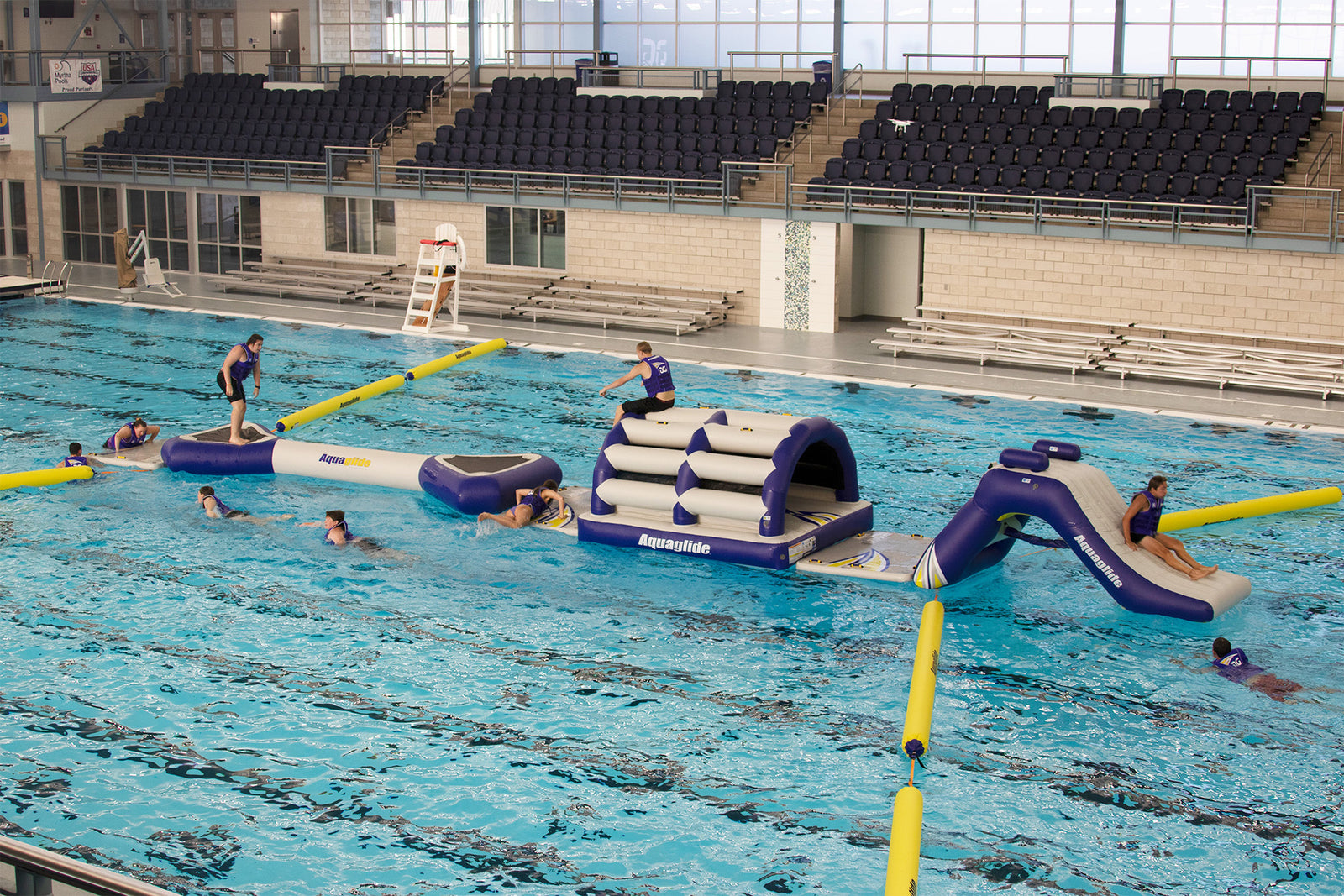 Indoor pool with inflatable obstacle course and people participating.