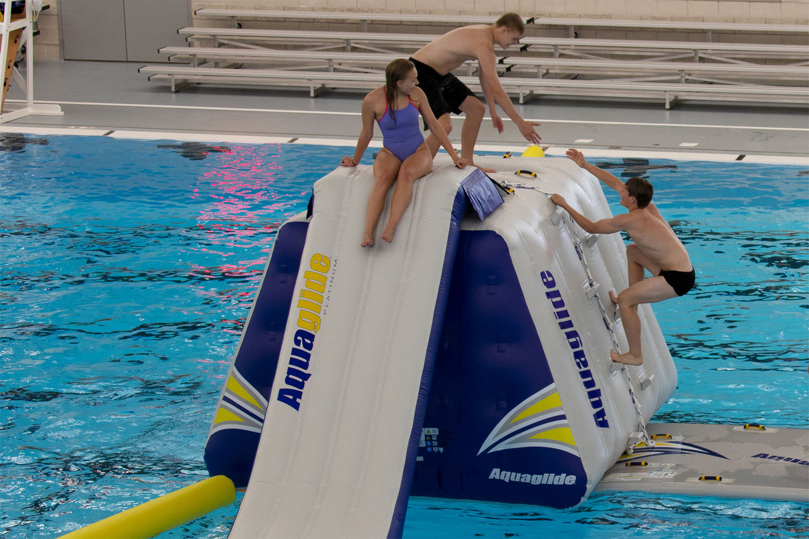 Three people climbing and sitting on an inflatable aqua slide in a pool.