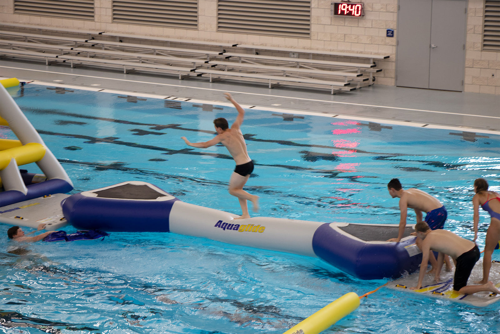 People play on inflatable obstacles in an indoor swimming pool.