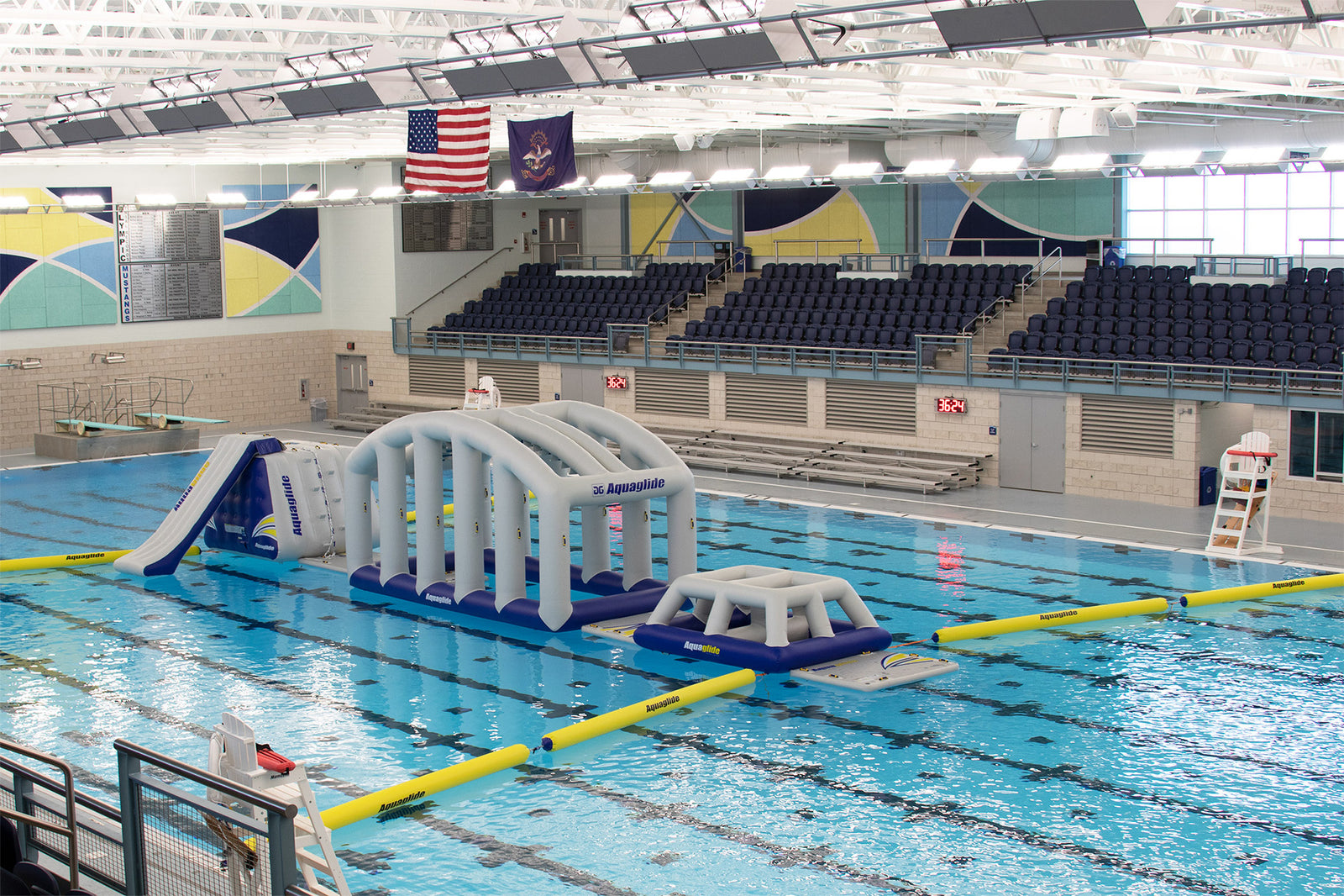 Indoor pool with inflatable obstacle course and empty spectator stands.