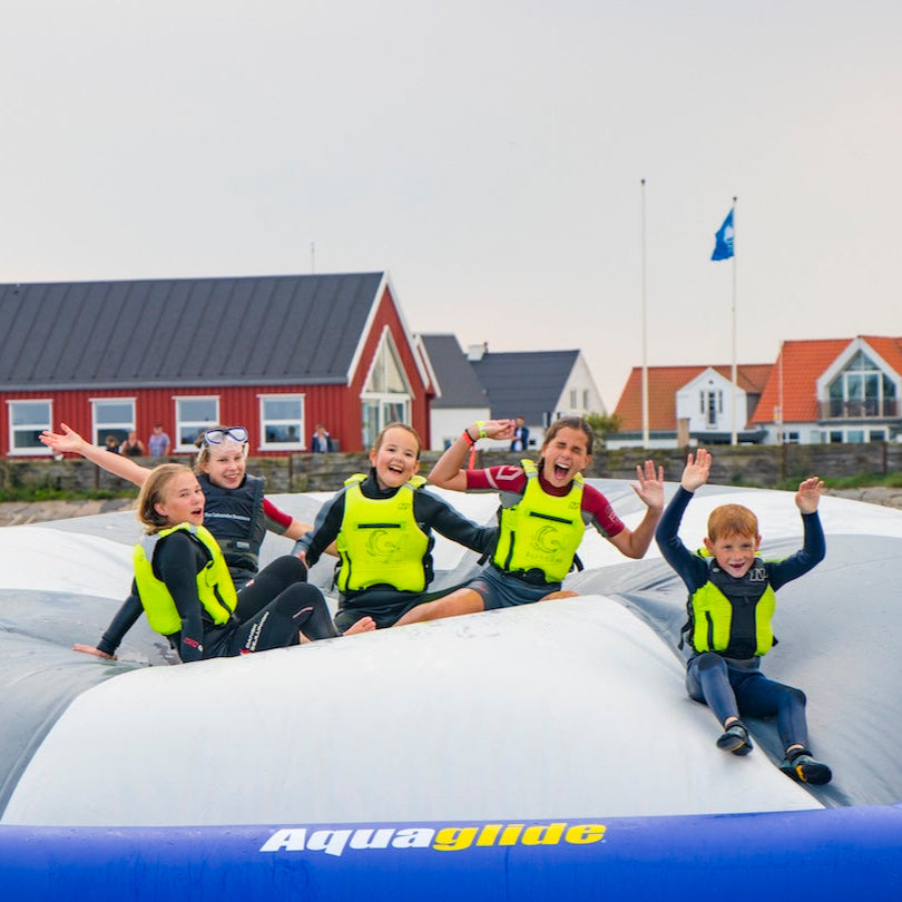 Group of kids in neon vests pose excitedly on the Kaos inflatable in front of red cottages.