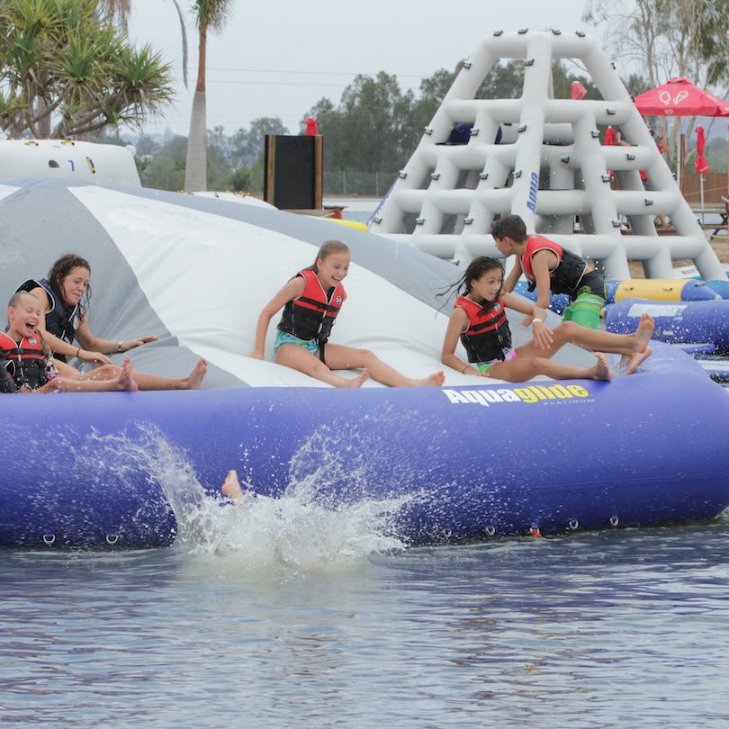 Group of kids laugh and slide on the Kaos inflatable while one splashes into the water below.