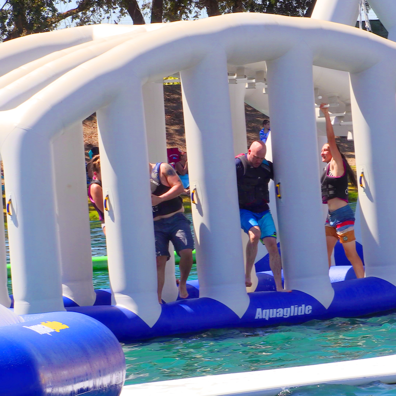 Adults navigate through the Monkey Dome inflatable, reaching and stepping through vertical bars.