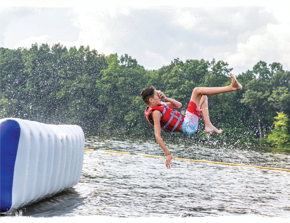 A kid jumping into the water wearing a PFD