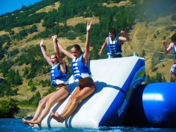 Two people delightfully plunge down the Plunge Slide, arms up, wearing life jackets.