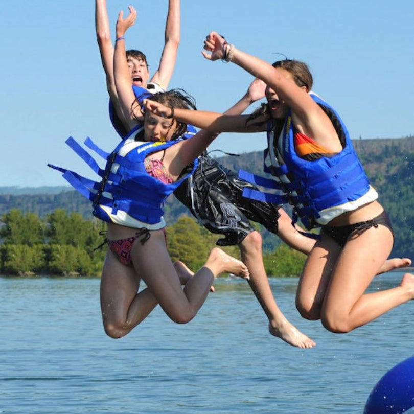 Three teens in life jackets jump from the Rebound 20 water bouncer.
