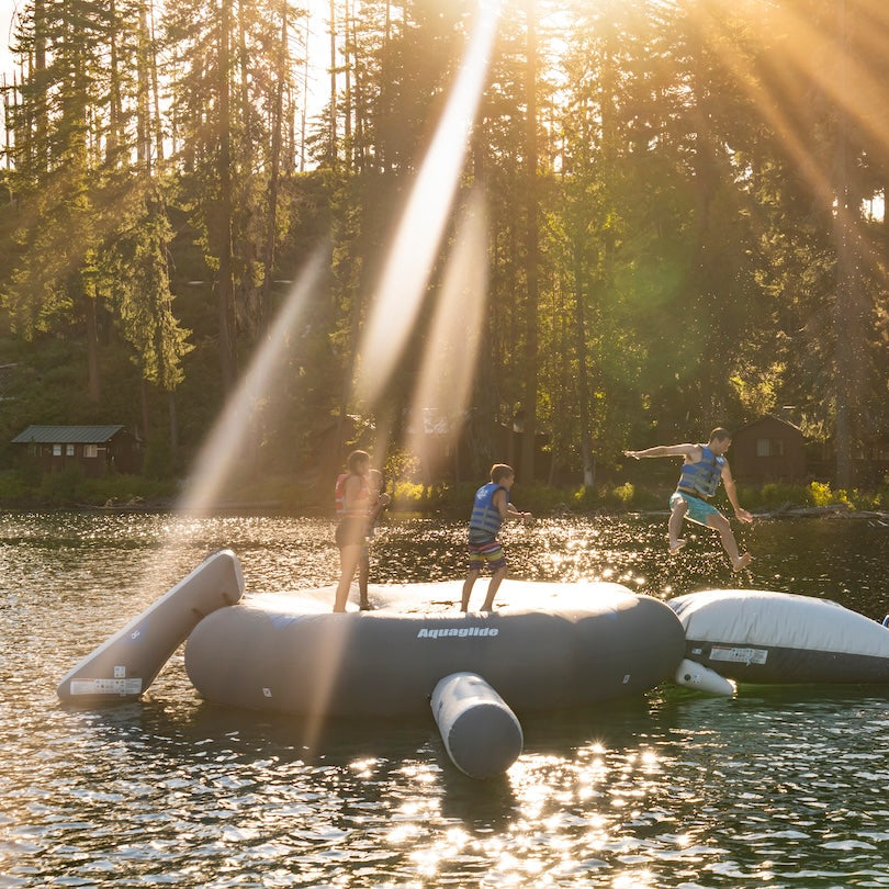 A group plays on the Large Ricochet / Recoil Slide on a lake at sunset.