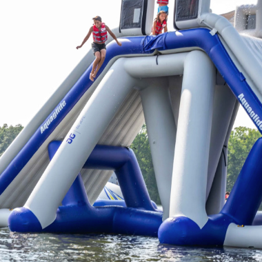 Person jumping off a large inflatable water structure into a lake.