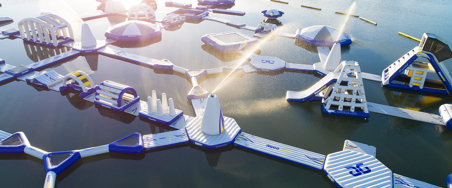 Floating inflatable water park with interconnected obstacle courses and slides on a calm lake.