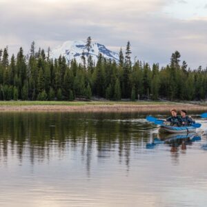 Two men paddle the Chinook 120 with pine trees and a snow covered mountain in the background