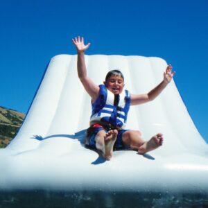 Young boy sliding down the free fall 6 with his arms up and a big smile