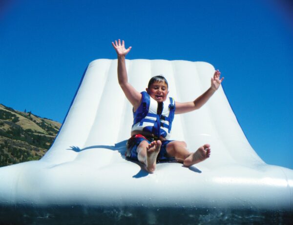 Young boy sliding down the free fall 6 with his arms up and a big smile