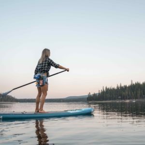 A woman paddles a Cascade away from the camera on a calm lake