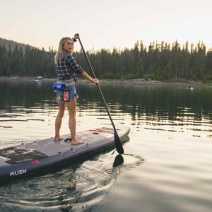 Woman paddling Kush SUP on calm lake while looking at the camera