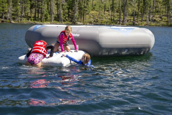 Young girls clamber onto a C Deck connected to a bouncer in the middle of a scenic lake