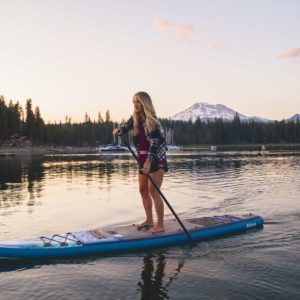 Woman paddles Roam SUP during sunset with mountains in the background