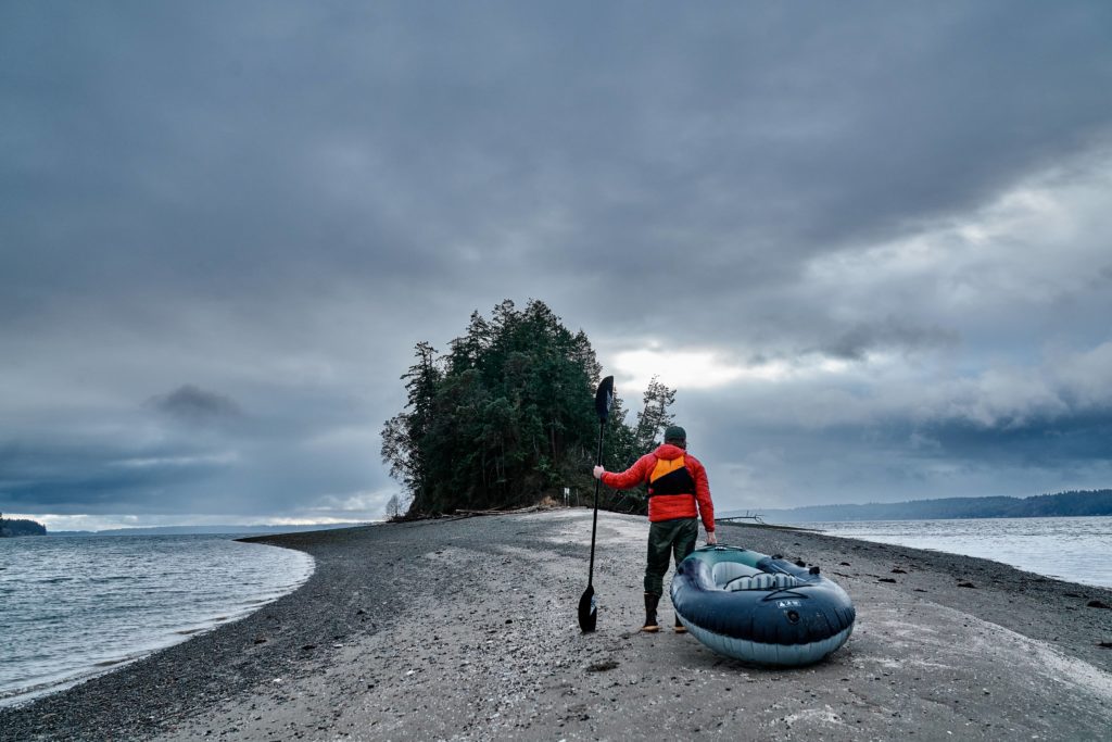 A paddler dragging an ultralight kayak up an island beach while looking towards dark clouds