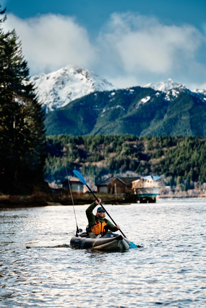Paddler in an inflatable fishing kayak with mountains in the background